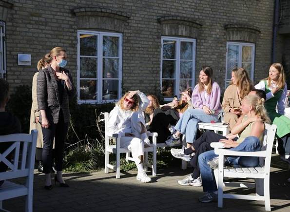 Statsminister Mette Frederiksen hilser på en gruppe unge kvinder, der sidder udenfor i solen på Vallekilde Højskole