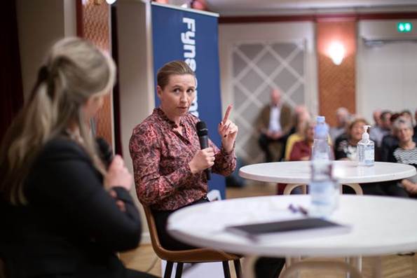 Statsminister Mette Frederiksen sidder ved et rundt bord. I hånden har hun en mikrofon, hvorfra hun svarer på spørgsmål fra Fyns Amts Avis