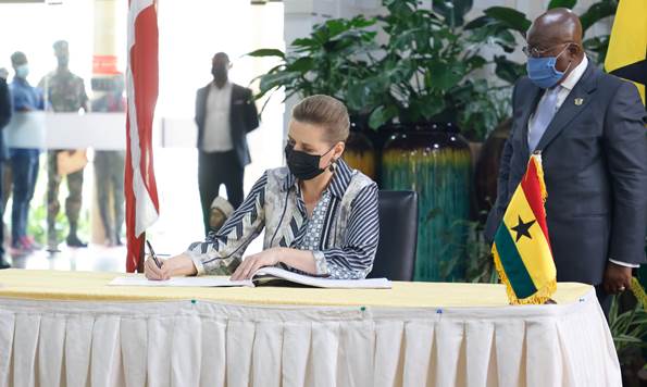 Statsminister Mette Frederiksen skriver i gæstebogen, mens Ghanas præsident står bagved