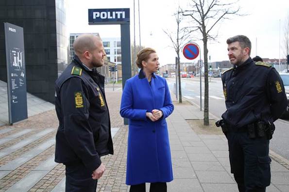 Statsminister Mette Frederiksen taler med to politibetjente ude foran en politigård i Aalborg