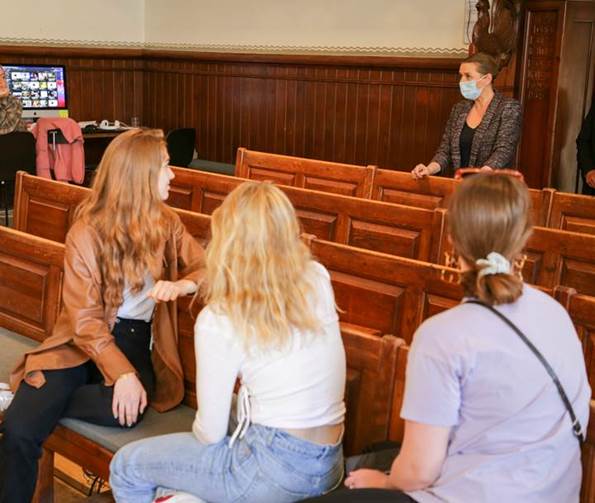 Statsminister Mette Frederiksen hilser på en gruppe elever, der sidder på bænke inde i en sal på Vallekilde Højskole.