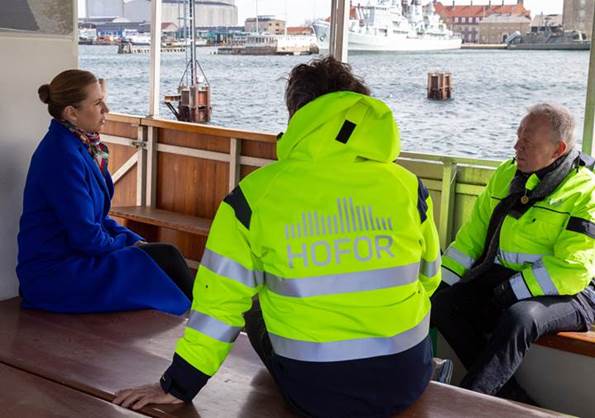 Statsminister Mette Frederiksen sidder og taler med to arbejdere ude på en båd. 