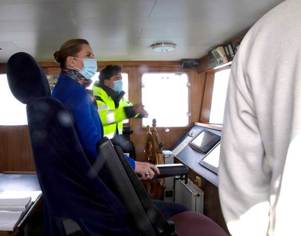 Statsminister Mette Frederiksen sidder ved roret ombord på et skib. 
