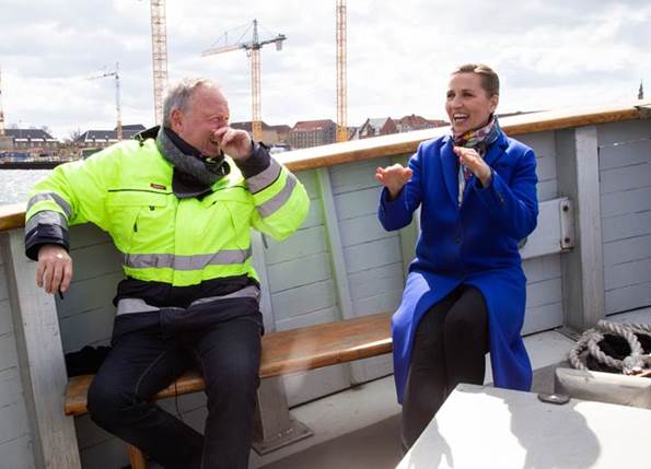 Statsminister Mette Frederiksen sidder og taler med en person iført refleksjakke. De sidder om bord på en båd.