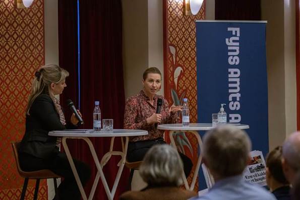 Statsminister Mette Frederiksen sidder ved et rundt bord. I hånden har hun en mikrofon, hvorfra hun svarer på spørgsmål fra Fyns Amts Avis