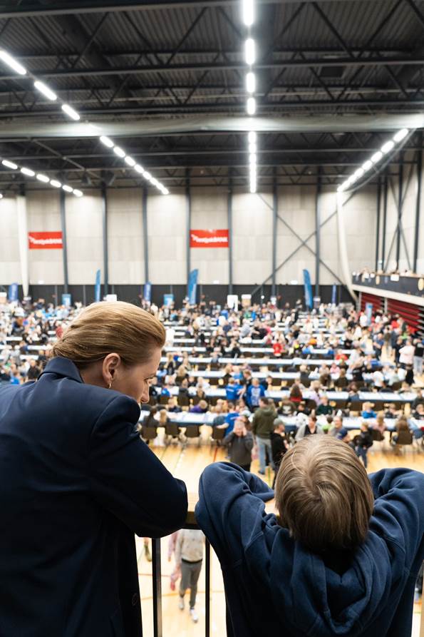 Statsminister Mette Frederiksen ved siden af en skoleelev der skuer ud mod deltagerne til Landsfinalen i Skolernes Skakdag